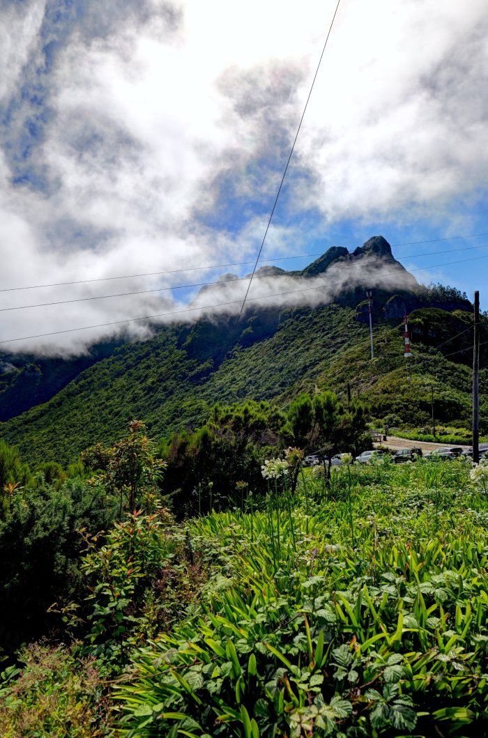 Veicoli parcheggiati in uno slargo verde con montagne coperte da nuvole sullo sfondo