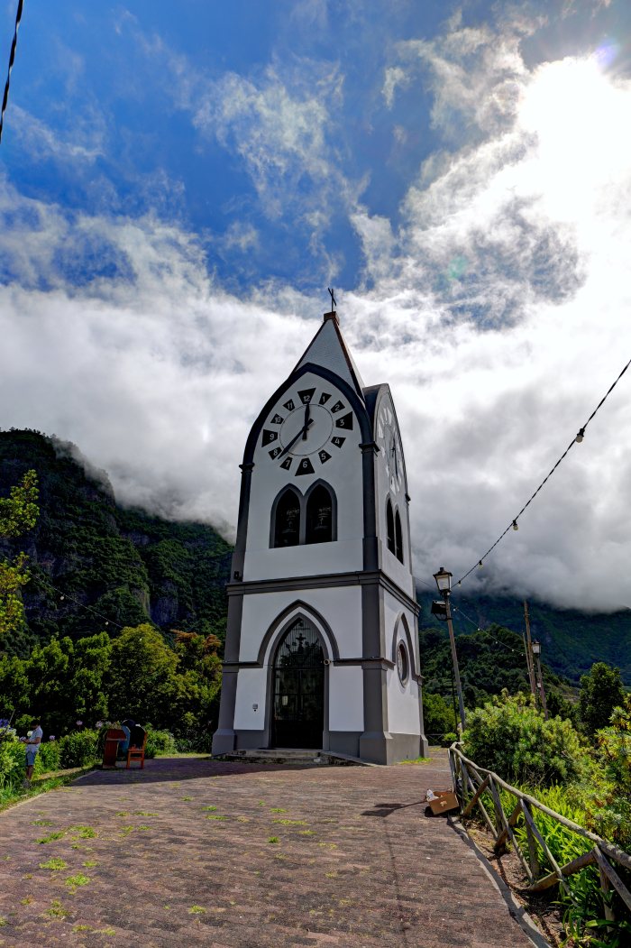 Due persone sedute vicino a un campanile con orologio, montagna verde sullo sfondo