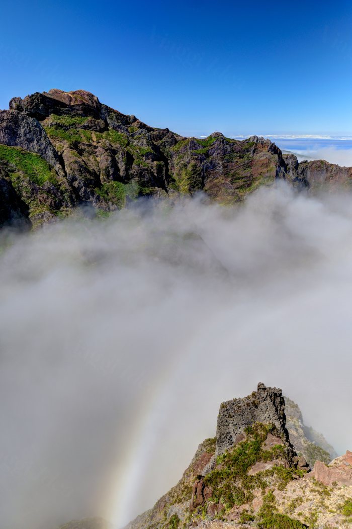 Montagne rocciose con nuvole e un arcobaleno pallido visibile fra le vette