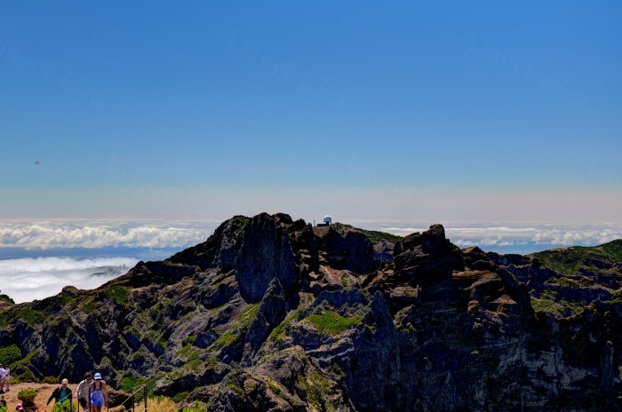 Turisti in cima a una montagna rocciosa con nuvole sotto