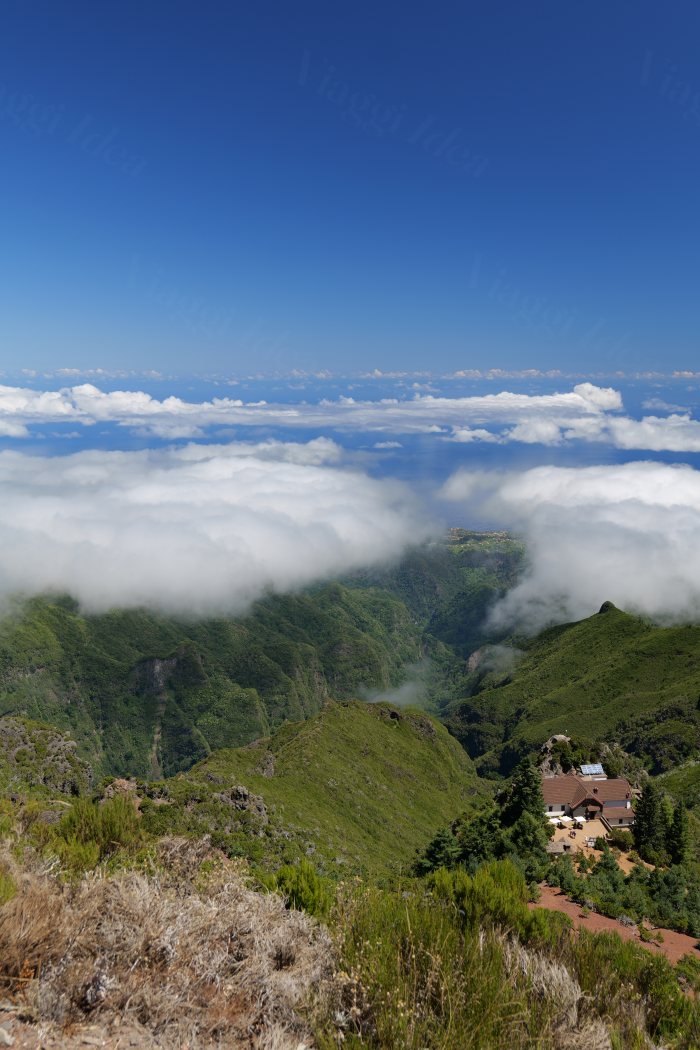 Vista panoramica su colline verdi fra le nuvole, con una casa in basso