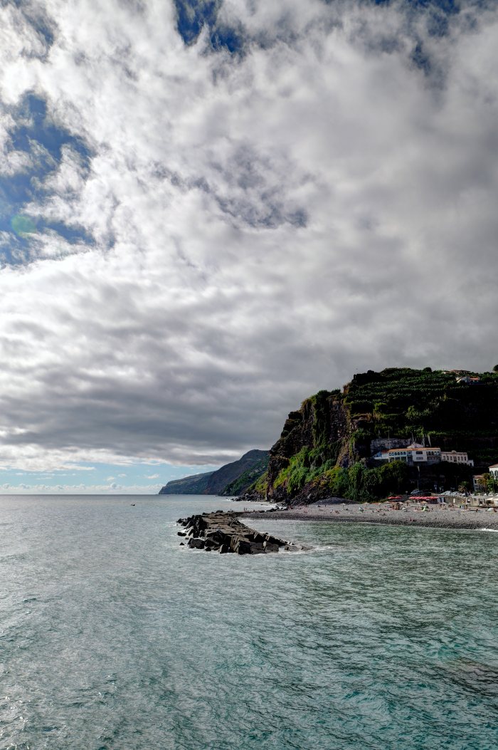 Persone in spiaggia accanto a un molo di pietra e colline verdi